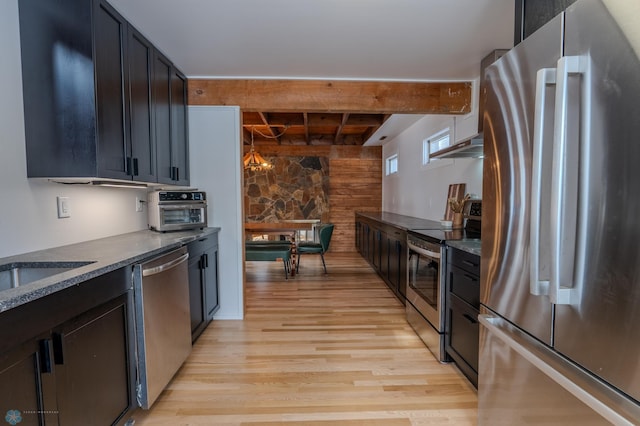 kitchen featuring sink, dark stone counters, beam ceiling, stainless steel appliances, and light wood-type flooring