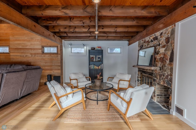 sitting room with beam ceiling, wooden walls, a fireplace, and light hardwood / wood-style floors