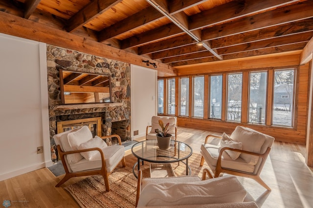 living area with a stone fireplace, wooden ceiling, beamed ceiling, and light wood-type flooring