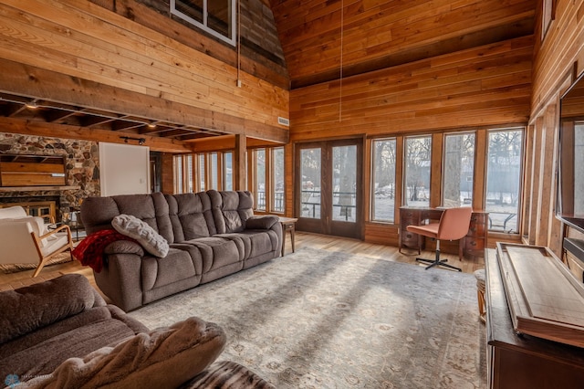 living room with french doors, a stone fireplace, wooden walls, a towering ceiling, and hardwood / wood-style floors