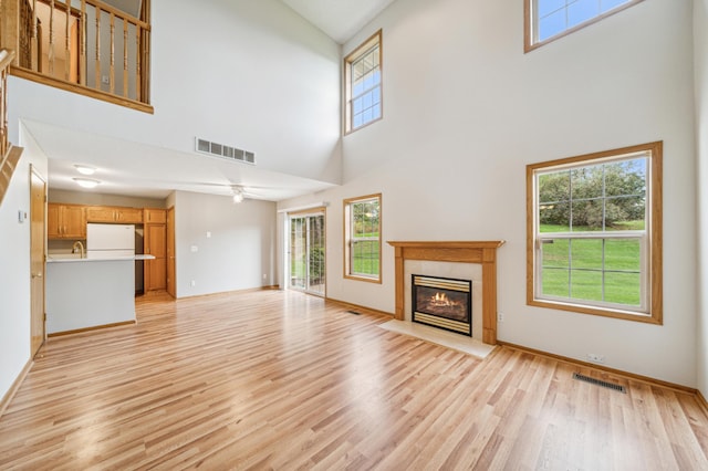 unfurnished living room featuring a high ceiling, ceiling fan, and light hardwood / wood-style flooring