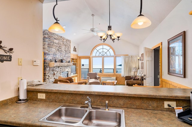 kitchen with vaulted ceiling, a stone fireplace, wood walls, sink, and hanging light fixtures