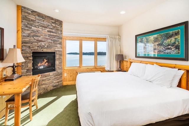 bedroom featuring a water view, a stone fireplace, and dark carpet