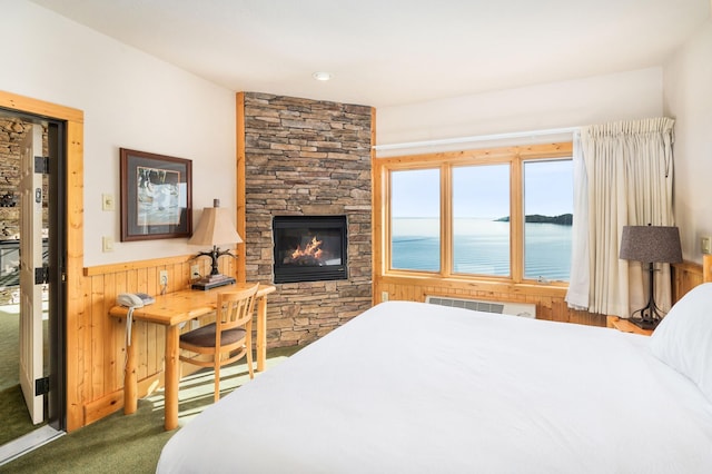 bedroom with wooden walls, carpet, a water view, a fireplace, and an AC wall unit