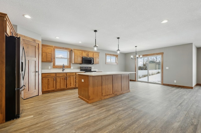 kitchen featuring stainless steel appliances, decorative light fixtures, a center island, and light hardwood / wood-style flooring