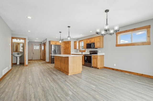 kitchen featuring appliances with stainless steel finishes, a center island, light wood-type flooring, and decorative light fixtures