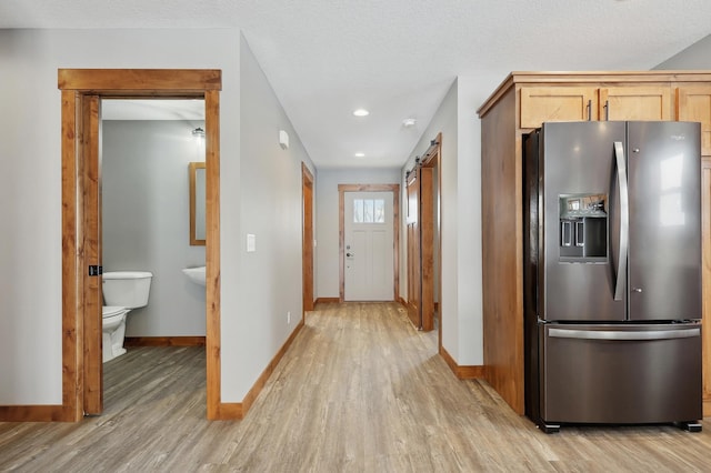 kitchen featuring stainless steel refrigerator with ice dispenser, a textured ceiling, light hardwood / wood-style flooring, light brown cabinets, and a barn door