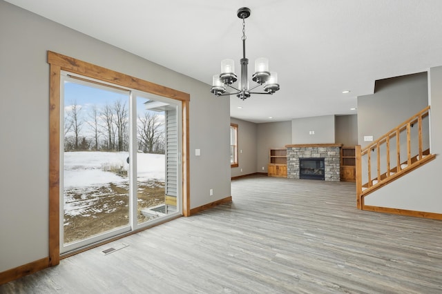 unfurnished living room with an inviting chandelier, a fireplace, plenty of natural light, and wood-type flooring