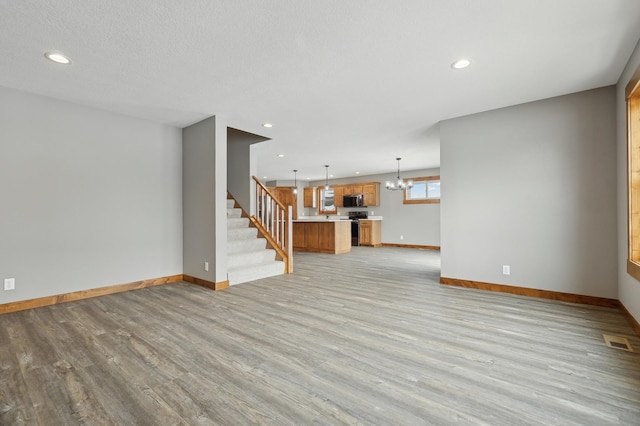 unfurnished living room featuring an inviting chandelier and light hardwood / wood-style flooring