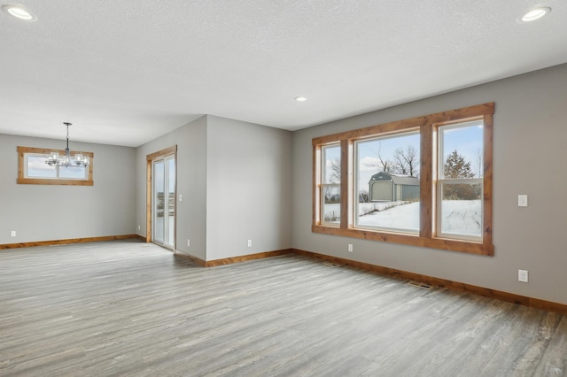 empty room with an inviting chandelier, a textured ceiling, and light wood-type flooring