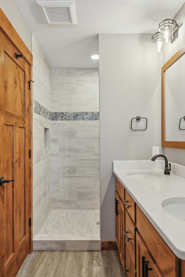 bathroom featuring vanity, wood-type flooring, a tile shower, and a textured ceiling