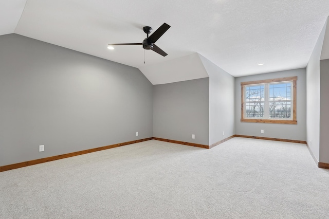 additional living space featuring a textured ceiling, vaulted ceiling, light colored carpet, and ceiling fan