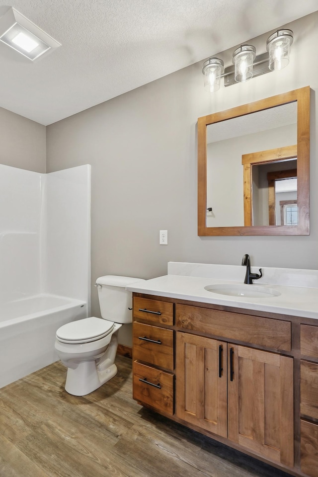 full bathroom featuring shower / bathing tub combination, hardwood / wood-style flooring, vanity, toilet, and a textured ceiling