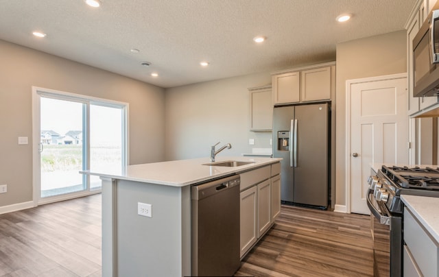 kitchen with sink, wood-type flooring, a textured ceiling, appliances with stainless steel finishes, and an island with sink