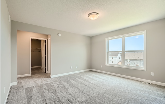 unfurnished bedroom featuring a walk in closet, a closet, light carpet, and a textured ceiling