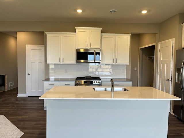 kitchen with sink, appliances with stainless steel finishes, white cabinetry, a kitchen island with sink, and decorative backsplash