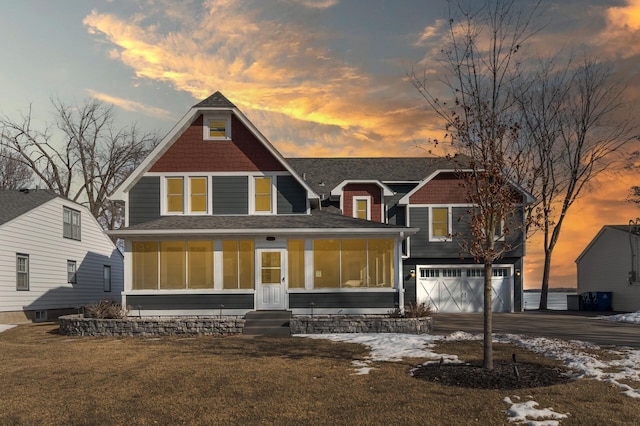 back of property featuring aphalt driveway, a garage, a shingled roof, and a sunroom