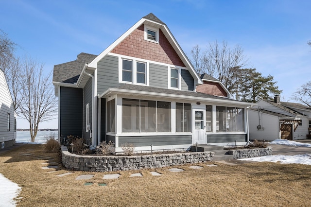 shingle-style home with a front yard, a sunroom, and a shingled roof