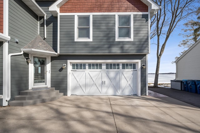 view of front of property featuring a garage, a water view, driveway, and a shingled roof