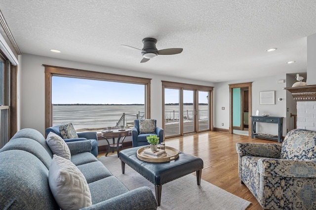 living area featuring a textured ceiling, wood finished floors, baseboards, a brick fireplace, and ceiling fan