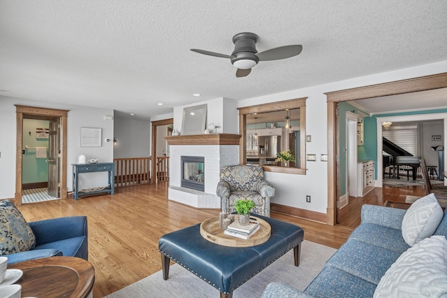 living area featuring baseboards, recessed lighting, wood finished floors, a glass covered fireplace, and a textured ceiling