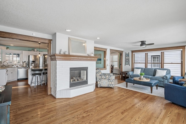 living room with a fireplace, ceiling fan, wood finished floors, and a textured ceiling