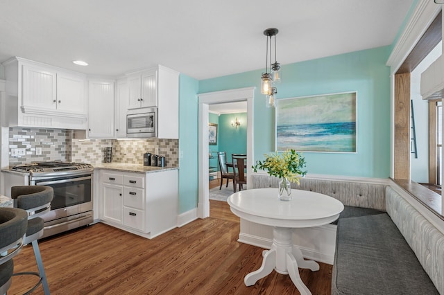 kitchen featuring backsplash, white cabinetry, stainless steel appliances, and wood finished floors