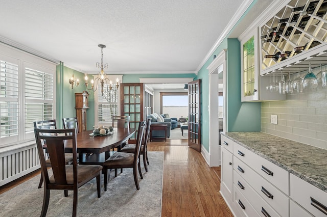 dining room featuring a textured ceiling, an inviting chandelier, wood finished floors, and crown molding