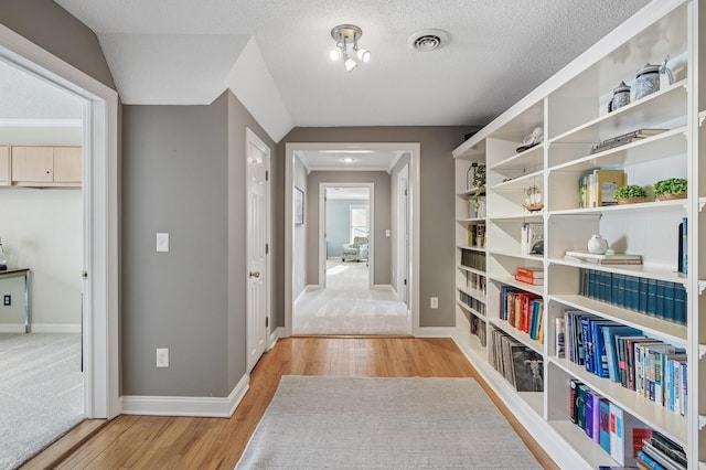 hall featuring visible vents, light wood-style flooring, a textured ceiling, and baseboards