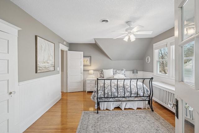 bedroom featuring a wainscoted wall, radiator, lofted ceiling, and wood finished floors