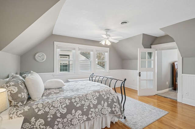 bedroom with visible vents, ceiling fan, a wainscoted wall, vaulted ceiling, and wood finished floors