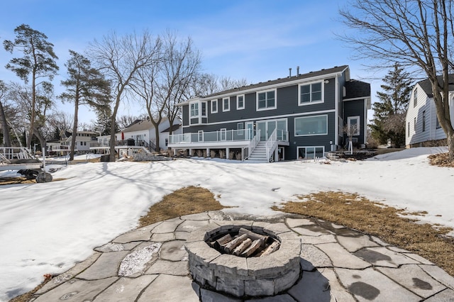 snow covered house with stairway, a fire pit, a deck, and a residential view