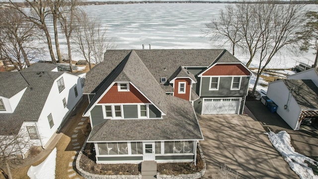 view of front of property with a sunroom, a shingled roof, concrete driveway, a garage, and a water view