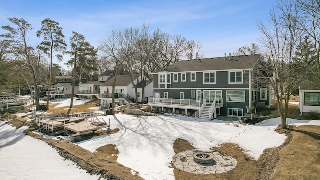 snow covered house featuring a deck, stairway, a fire pit, and a residential view