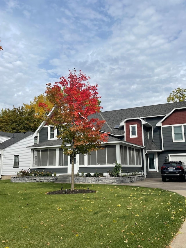 view of front of home featuring a shingled roof, a front yard, and a sunroom