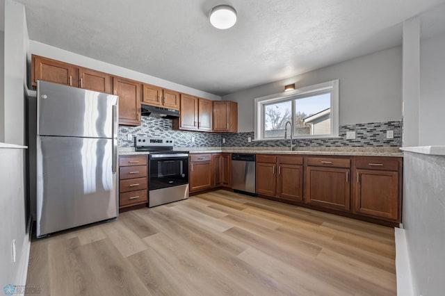 kitchen with sink, appliances with stainless steel finishes, backsplash, light stone countertops, and light wood-type flooring