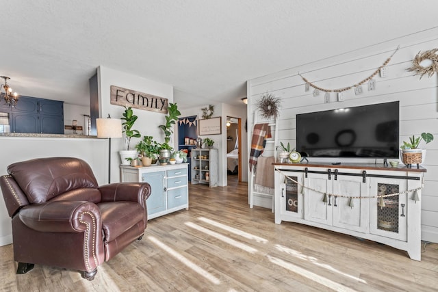 living room with wooden walls, a chandelier, a textured ceiling, and light wood-type flooring