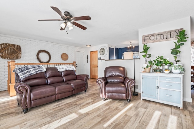 living room featuring ceiling fan with notable chandelier, brick wall, and light hardwood / wood-style floors