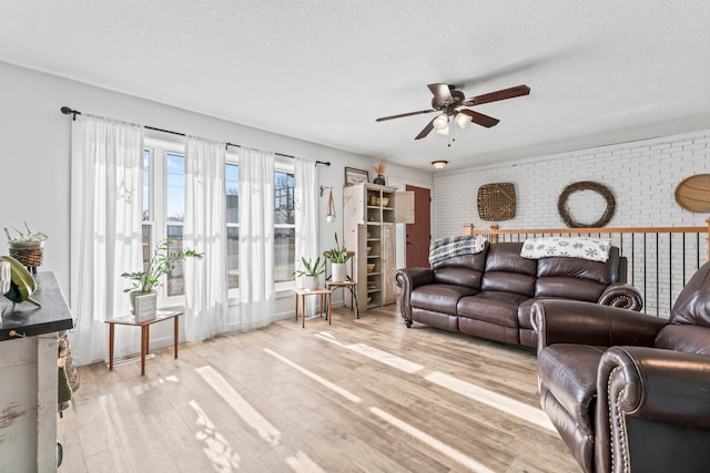 living room featuring ceiling fan, brick wall, light hardwood / wood-style floors, and a textured ceiling