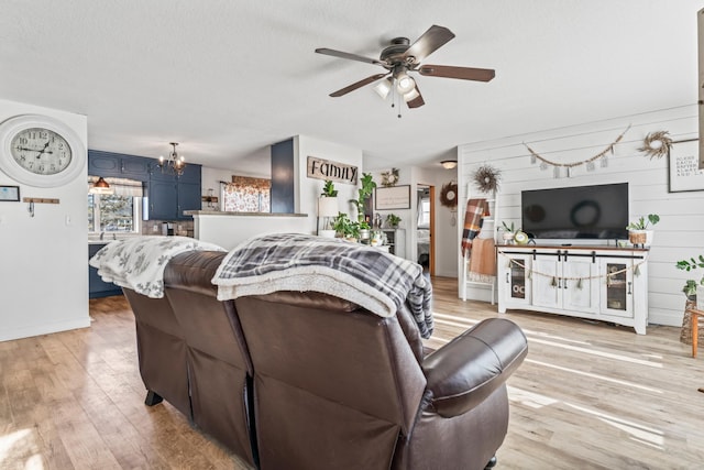 living room featuring ceiling fan with notable chandelier, a textured ceiling, and light wood-type flooring