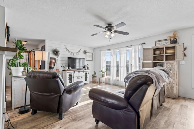 living room featuring ceiling fan, a textured ceiling, and light wood-type flooring