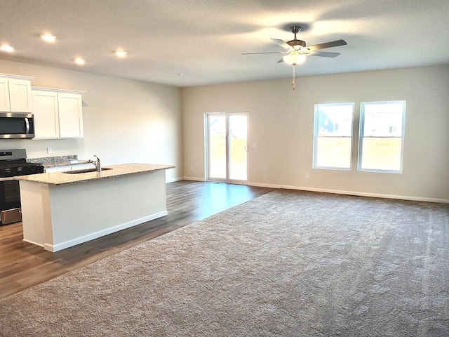 kitchen with sink, white cabinetry, stainless steel appliances, light stone counters, and a center island with sink