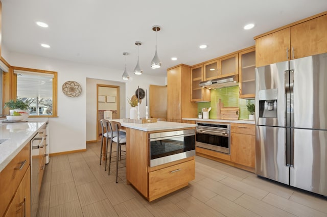 kitchen with a breakfast bar area, hanging light fixtures, stainless steel appliances, a center island, and decorative backsplash