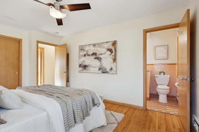 bedroom with light hardwood / wood-style flooring, ceiling fan, baseboard heating, tile walls, and ensuite bathroom