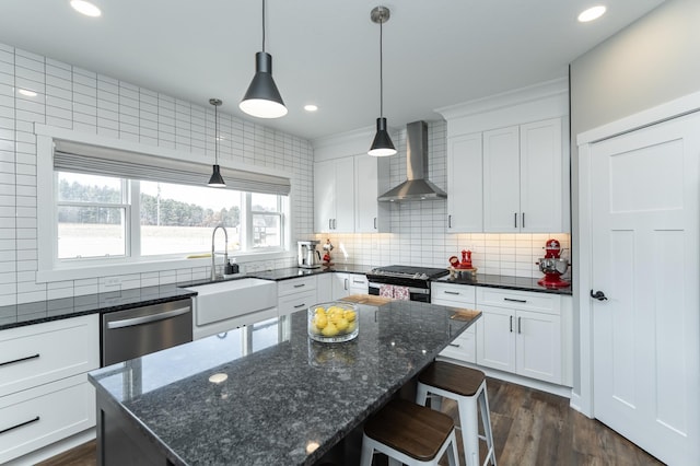 kitchen featuring appliances with stainless steel finishes, sink, dark stone countertops, a center island, and wall chimney exhaust hood