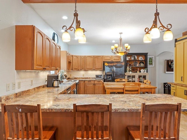 kitchen with kitchen peninsula, a barn door, stainless steel refrigerator with ice dispenser, a kitchen bar, and decorative backsplash