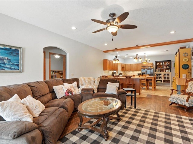 living room with ceiling fan with notable chandelier, light wood-type flooring, and a textured ceiling