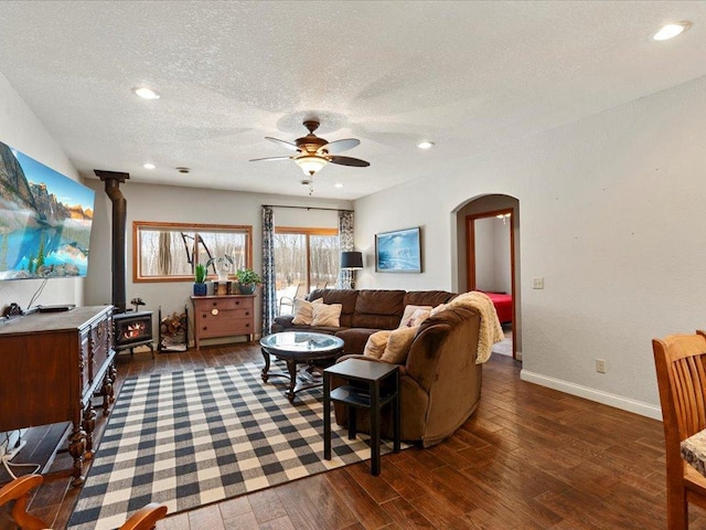 living room featuring ceiling fan, a wood stove, a textured ceiling, and dark hardwood / wood-style floors