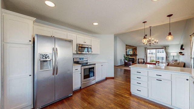 kitchen featuring appliances with stainless steel finishes, a large fireplace, white cabinets, and decorative light fixtures