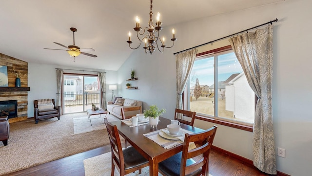 dining area featuring ceiling fan, a stone fireplace, vaulted ceiling, and dark wood-type flooring